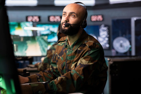 Army telecommunication systems agent in command center using radio and satellite gear, providing...
