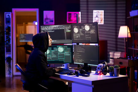 Hooded hacker in neon lit lair using PC to gain unauthorized network access, targeting unpatched connections. Rogue engineer at home bypassing security and exploit servers for stolen data profitの写真素材