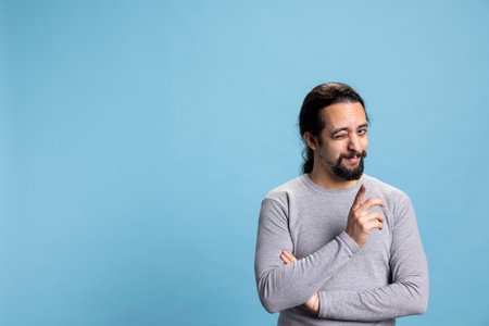 Joyful confident adult winking and telling jokes against blue background, acting cool with a vibrant authentic attitude. Young smiling person being flirty and playful, self assured man.の写真素材