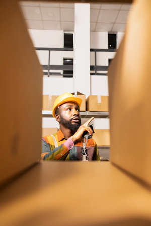 Employee in coveralls prepares parcels by scanning labels, ensuring shipment accuracy and efficient...