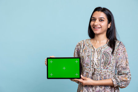 Positive happy girl presenting chroma key isolated screen on device, doing promotion for a commercial against studio background. Upbeat indian person used for advertising brands.の写真素材