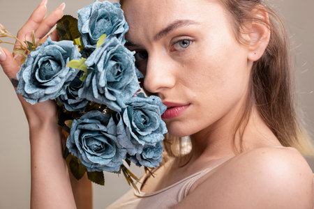 Radiant model with natural makeup and glossy skin holds blue roses bouquet, expressing wellness and calm. Her natural beauty and confident look ideal for skincare and self love campaigns.の写真素材