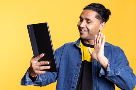 Friendly adult enjoying an entertaining conversation with friends on web call, laughing and feeling happy during video call meeting against studio background. Waving hand on camera.の写真素材