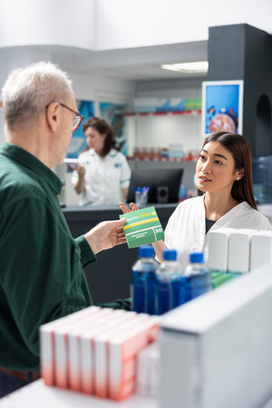 Retired man receives guidance from asian pharmacist in drugstore, discussing prescription medicine and supplements for wellness. Diverse people reviewing various medicaments on shelves.の写真素材