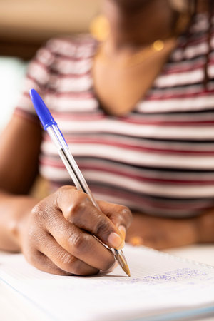 Black woman entrepreneur with pen in hand, writing project ideas on notebook during brainstorming moment. Close up of female individual organizing daily schedule and working remotely from home.の写真素材