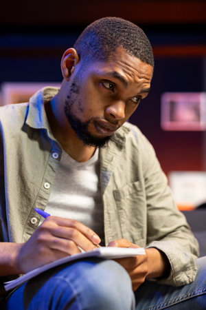 Focused person manages research by taking notes from online articles, working remotely on the couch...