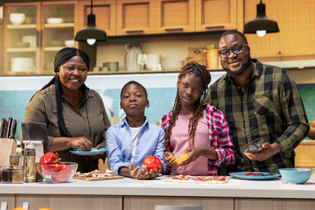 Portrait of african american family cooking homemade pizza together in a bright kitchen, having...