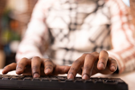Fingers of black man actively typing on keyboard while sitting at table. African American remote worker writing blog content, business emails and marketing documents from home.の写真素材