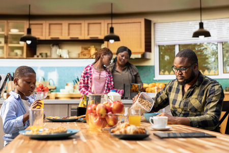 Black sweet family sharing croissants and orange juice in the morning, serving a rich colorful breakfast together under morning light. Young parents preparing the meal for their kids.の写真素材