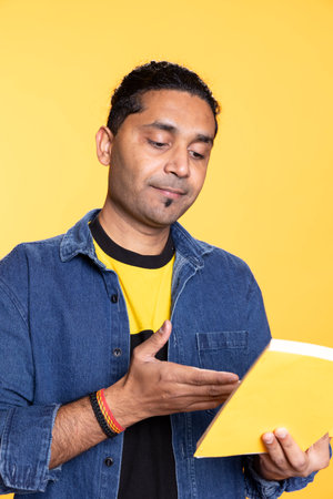 Young man book lover absorbed in a fantasy book against studio background, relaxing with a joyful story. Indian person enjoying lecture in front of the camera, reading enthusiast nerd.の写真素材