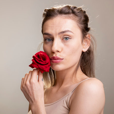 Powerful feminine model holding a red rose for a beauty ad in the studio, symbolizing self acceptance and glowing skin. Confident young woman with radiant natural look, self love.の写真素材