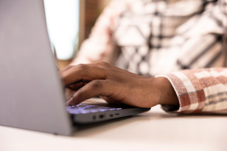 Close up on black man typing on laptop keyboard, updating online blog post. African american male individual seated at desk, using digital device to write business reports and gather financial data.の写真素材