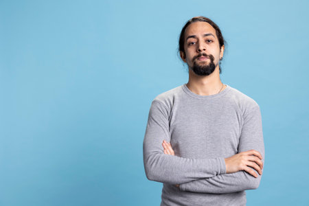 Male model with long curly hair posing with confidence in studio, standing with his casual wear against blue background. Young peaceful confident man with self assured attitude.の写真素材