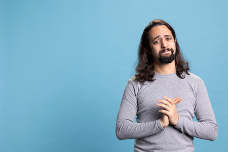 Spiritual guy praying to God and asking for forgiveness in studio, holding hands in a prayer. Hopeful person with belief in Christianity and religious meditation on camera.の写真素材
