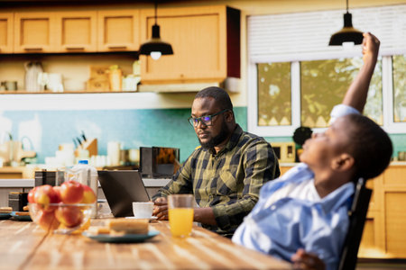 Father working on his laptop and serving breakfast with his cute family, gathered in the kitchen to enjoy the simple comfort of morning togetherness. Happy start to the day with sunlight.の写真素材
