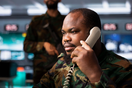 Army dispatcher looking at radar surveillance transmission on screens, relaying data to troops during telephone call. Military professional transmitting reconnaissance info to allies using phoneの写真素材