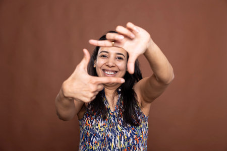 Happy female model making imaginary camera frame with her fingers. Cheerful Indian woman posing...