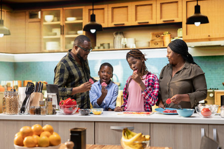Parents and children having fun in the kitchen cooking homemade pizza, layering ingredients like...
