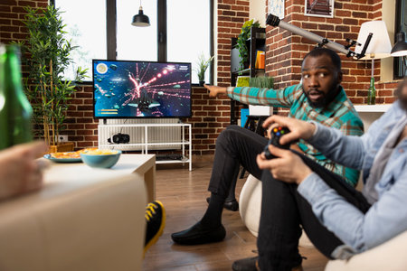 African american and caucasian men supporting each other and competing in multiplayer video game at...