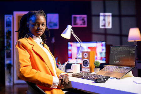 Portrait of programmer at desk typing code on laptop, developing software programs, entering commands. African american woman at home fixing errors in application, implementing new featuresの写真素材