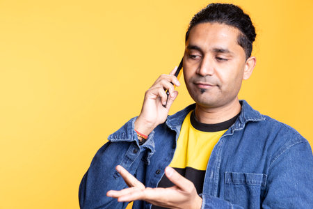 Upbeat indian person discussing with people during telephone call, casual clothing against orange background. Young friendly adult chatting with his friends on mobile phone line, lifestyle.の写真素材