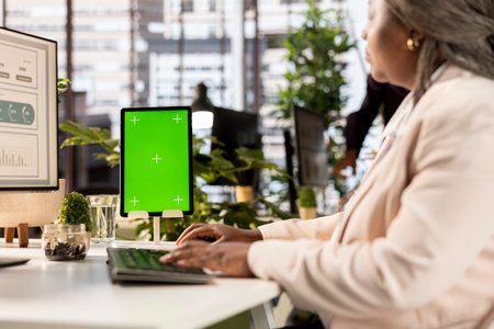 Company worker studies performance metrics next to green screen, networking and examining data analytics for a financial report. Female employee ensures corporate development.の写真素材