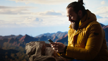 Trekker enjoys a quiet moment in the mountains scrolling phone app, where the high altitude air and breathtaking view encourage mindfulness. Relaxation and self improvement.の写真素材