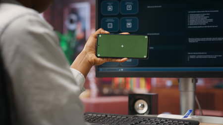 Woman using green screen smartphone to learn how to use AI LLM chatbot on computer screen in home office. Person watches video tutorial on mockup phone about artificial intelligence chatbots, camera Bの写真素材