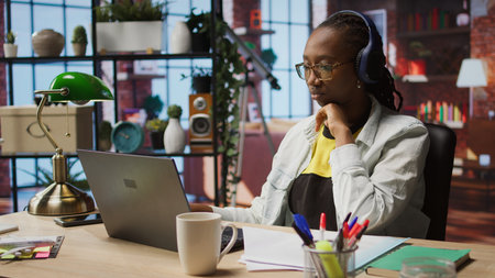 Teleworker listening music while typing on notebook keyboard in home office, writing emails. Remote...