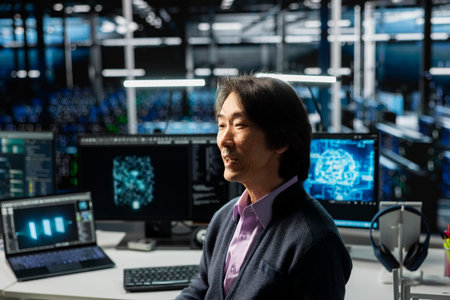 System administrator in data center using PC, managing AI training datasets. Asian man using...