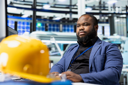 Male factory consultant observes production systems on a pc in a solar plant, providing expert feedback on efficiency, safety and sustainability aligned with green energy initiatives.の写真素材