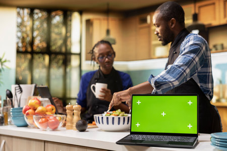 Isolated mockup laptop next to couple doing meal prep in the kitchen, man and woman cooking and...