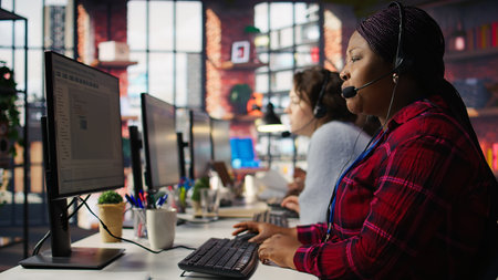 IT support expert at PC in call center office troubleshoots errors to minimize downtime. Tech support agent at desk writing code, maintaining technical systems and infrastructure, camera Bの写真素材