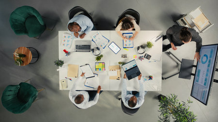 Top down view of diverse colleagues and managers participating in briefing. Business meeting focuses on negotiation, reporting and resource allocation for corporate development and success.の写真素材