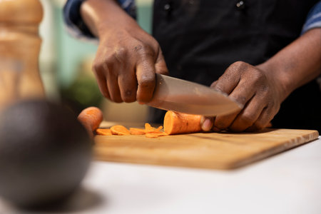Close up of african american man cutting carrots for a fresh salad, preparing organic ingredients on...