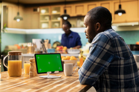 Green screen mockup on tablet with African American man enjoying breakfast at the table while...