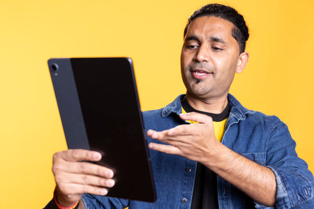 Young person with man bun waving his hands at the online meeting with his friends, communicating and laughing with people on web video call. Using tablet to enjoy a teleconference.の写真素材