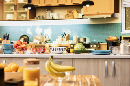 Empty kitchen with wooden dining furniture and modern appliances. Countertop displays colorful vegetables, fresh fruits and spices, representing a stylish home with cozy atmosphere.の写真素材
