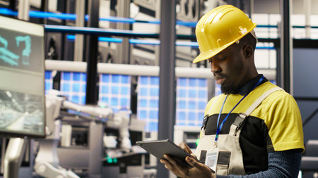 Smart factory mechanic using tablet to analyze IoT sensors data before modifying gear. African...
