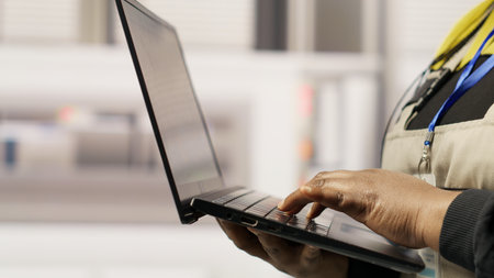 Technician in sustainable industrial plant monitors production equipment using laptop, diagnosing...