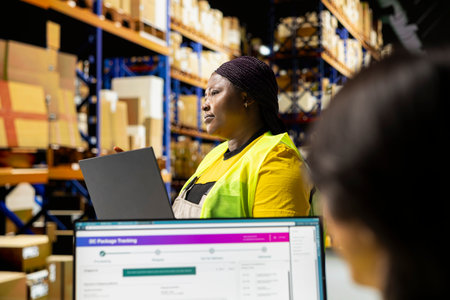 Worker reviewing products and organizing parcels on laptop in a startup warehouse. Storage racks full of merchandise and tech systems tracking deliveries, shipping in-house.の写真素材