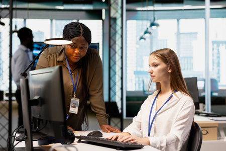 Manager supervising young employee in startup office, reviewing code scripts on computer. African american tech company supervisor overseeing work by trainee doing software developmentの写真素材
