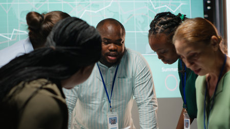 Diverse coworkers team participating in a late night briefing session, exchanging documents and reviewing finance updates. Aligning objectives through collaborative problem solving. Camera B.の写真素材