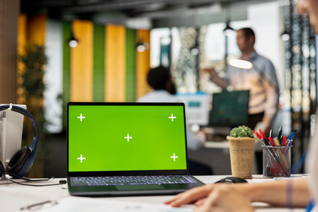 Close up of laptop with blank chroma key display on desk in modern office. Caucasian professional uses device with isolated green screen template while working corporate workspace.の写真素材