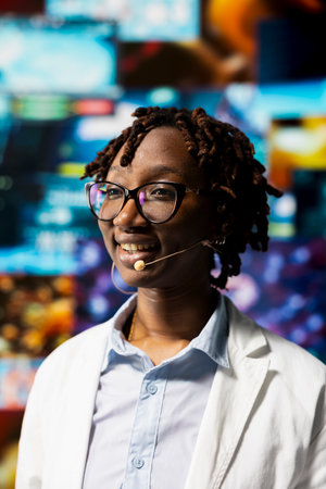 Smiling researcher talking in mic during presentation, reviewing data analytics. Jolly woman in medical research lab showing health data to audience on videowallの写真素材