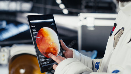 Close up of astronaut using tablet to check Mars telemetry data during human expansion in space mission. Cosmonaut in starship analyzes red planet surface supporting mankind survivalの写真素材
