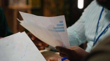 Close up of diverse staff collaborating on data forecasting and analysis, exchanging documents late in the office. Updating stakeholders with predictions and other business intel. Camera B.の写真素材