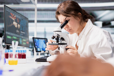 Close up of histology technician in lab using scientific microscope for cellular analysis. Woman...