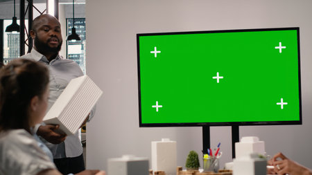 Property engineers team study architectural blueprints with a mockup on TV, collaborating in urban development master plan. Modern residential project with infrastructure goals.の写真素材