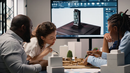 Real estate professionals engage in meeting to review blueprints and 3D models, planning for a large scale urban development project aimed at housing and infrastructure growth.の写真素材